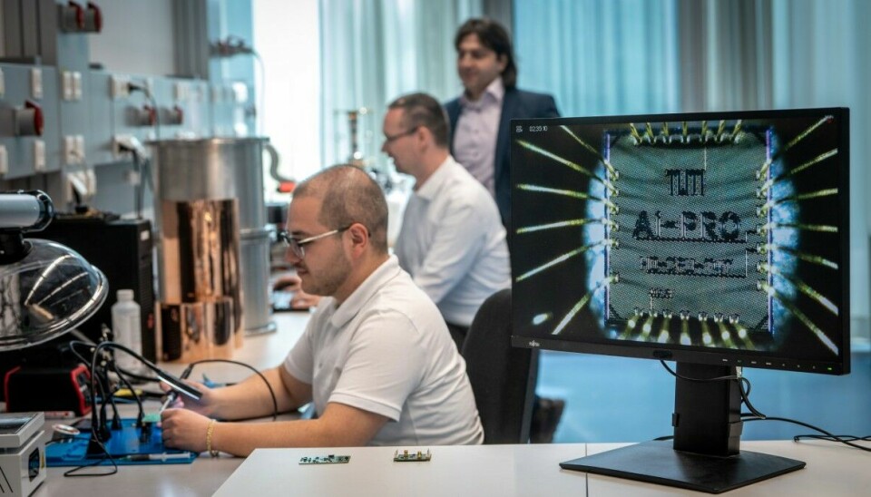 The research team with Prof. Hussam Amrouch in the background. In the foreground, a view of the chip under the microscope. Das Forschendenteam mit Prof. Hussam Amrouch im Hintergrund. Im Vordergrund eine Ansicht des Chips unter dem Mikroskop.